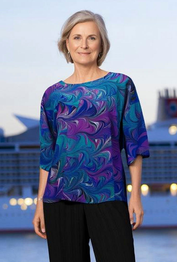 Woman wearing a marbled silk top with black pants against the backdrop of a cruise ship