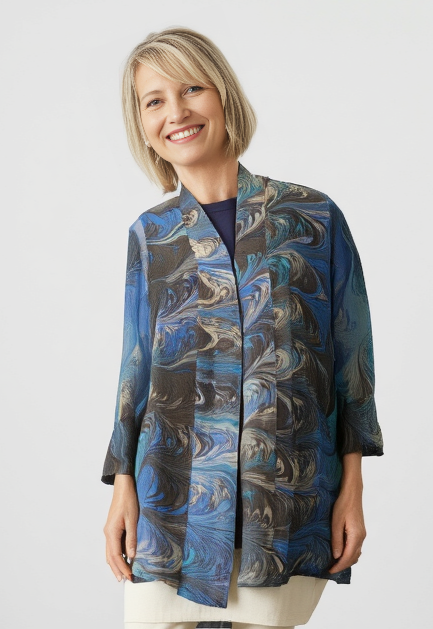 Woman wearing a blue and brown marbled silk jacket and white pants against a plain background
