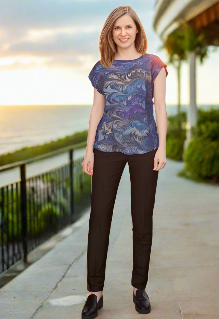 Woman wearing a teal and gray marbled silk top and black pants standing on a rooftop with a sunset view.