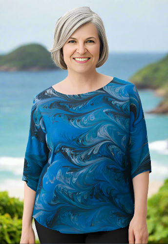 Woman wearing a blue marbled silk top with a scenic background of water and greenery.