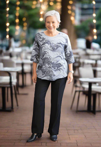 Woman wearing a patterned top and black pants standing indoors.