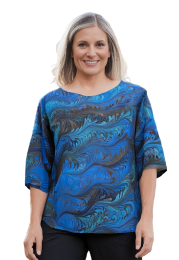 Woman wearing a mint and brown marbled silk top and black pants standing on a sidewalk with trees in the background.