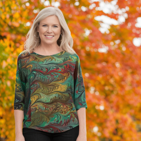 Woman wearing a colorful patterned shirt standing in front of autumn foliage.