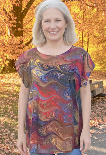 Woman standing in a park wearing a marbled silk top with autumn leaves and trees in the background
