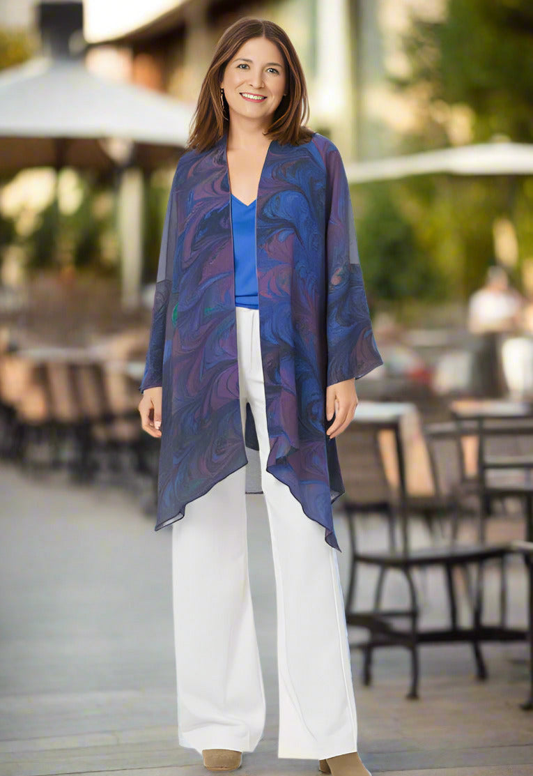 Woman wearing a blue patterned wrap -style garment over a blue top and white pants at an outdoor restaurant