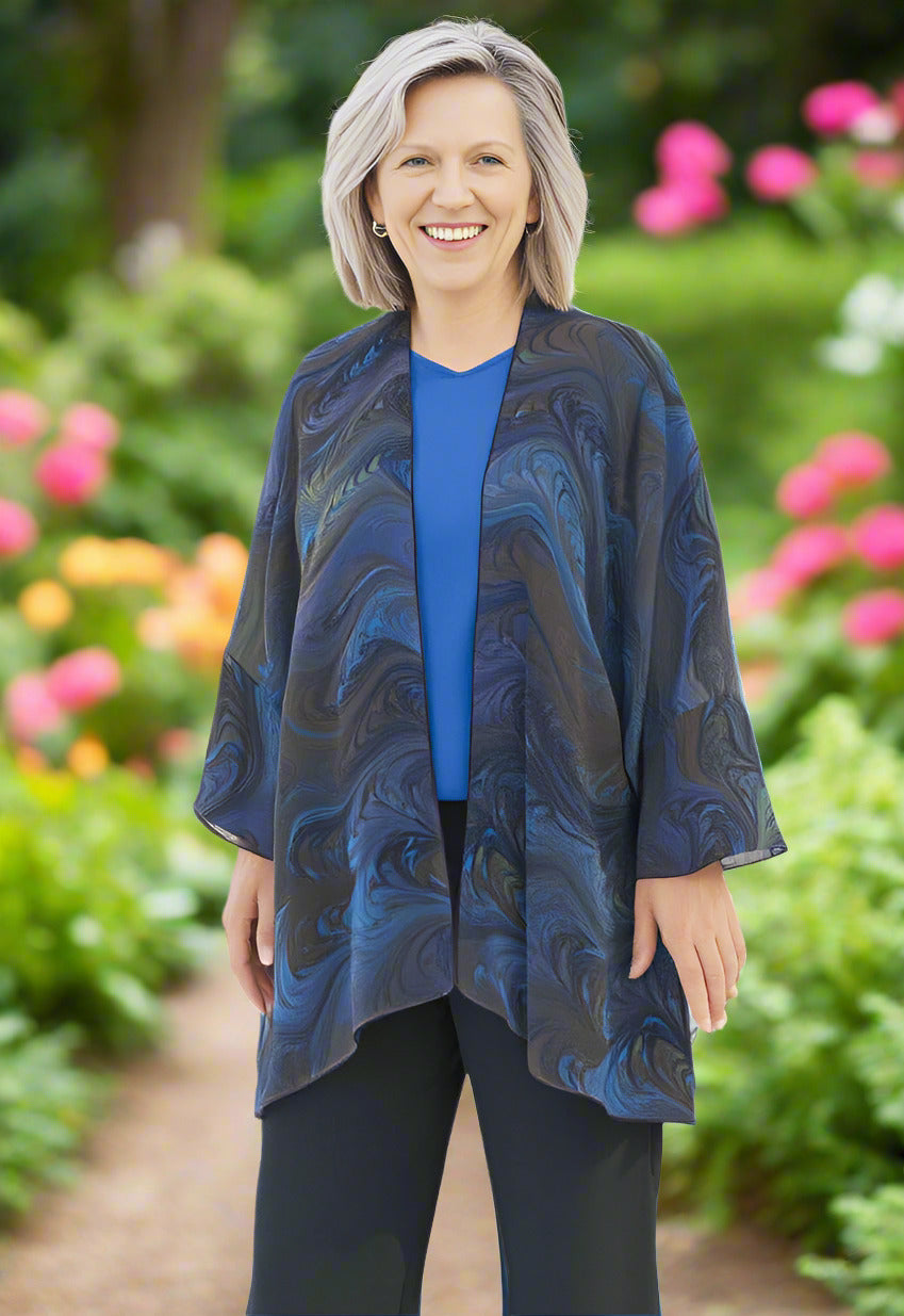 Woman wearing a blue and brown hand marbled patterned wrap style jacket in a botanical garden setting