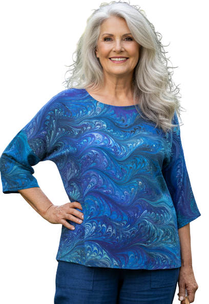 Woman in a blue marbled silk top and pants standing in a garden with flowers and plants.