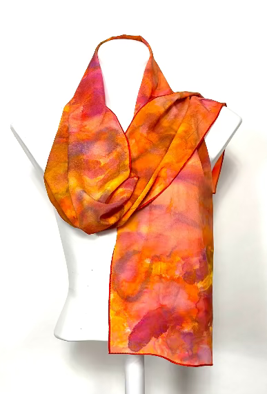 Orange and coral hand painted patterned scarf on a white mannequin against a white background