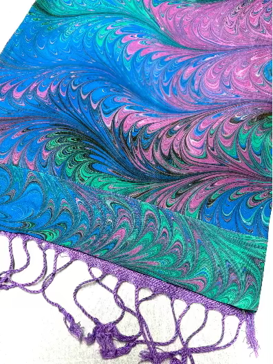 End of a marbled silk scarf in colors purple, blue, and green with the violet lining and trim showing