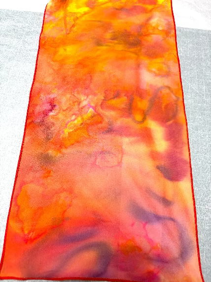Closeup of a colorful hand painted scarf with orange, pink, and purple hues 