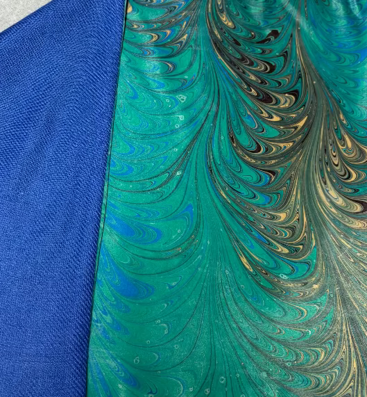 Close-up of a scarf with blue and green marbled pattern and turned to show the bright blue lining of this scarf