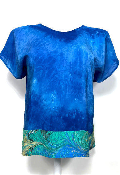 Blue hand dyed shirt with a marbled green and blue hem on a white background