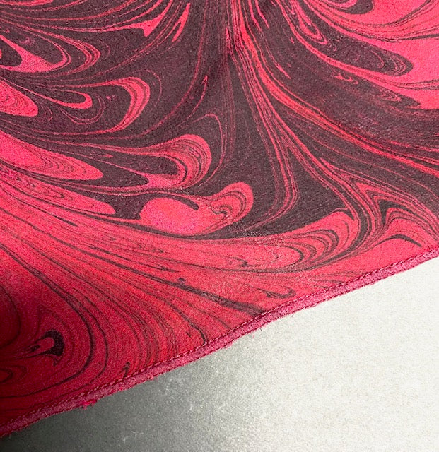 Marbled silk scarf edge with red and black swirly pattern on a white background