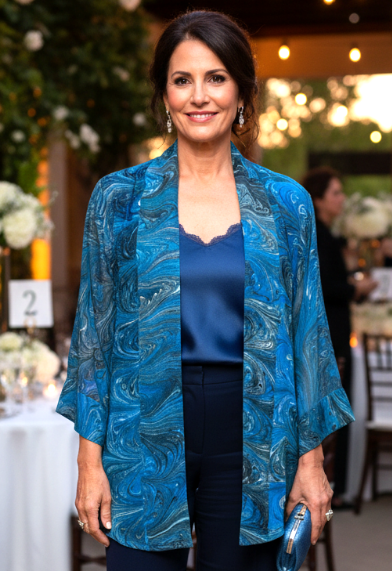 Woman in a blue marbled silk kimono jacket and pants standing in an outdoor event setting with tables and decorations.