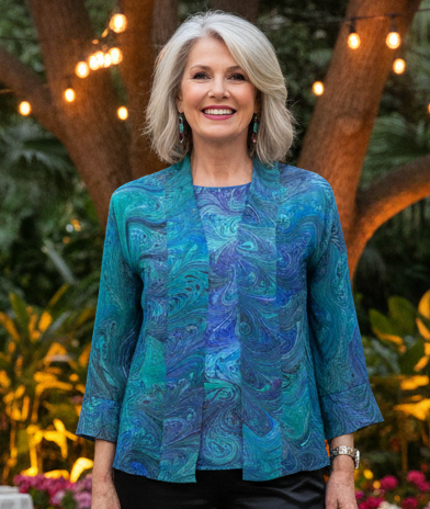 Woman in a blue marbled silk top and kimono jacket standing in an outdoor setting with floral decorations and string lights.