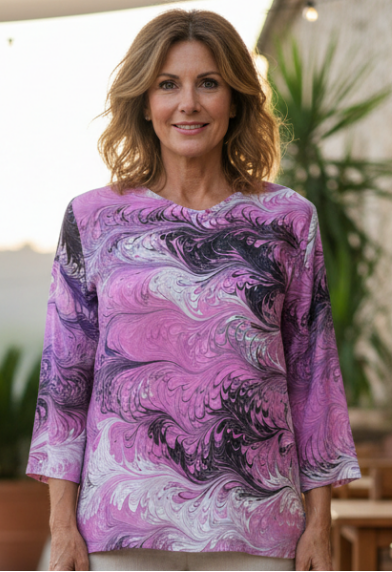 Woman wearing a marbled silk pink patterned top standing in an outdoor setting with tables and chairs.
