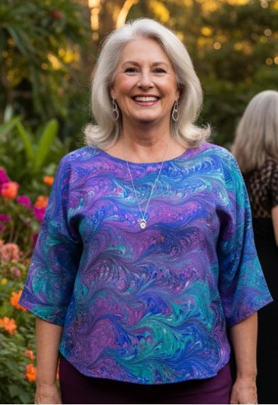 Woman in a colorful marbled silk top in blue, green and violet colors standing in a garden with other people in the background.