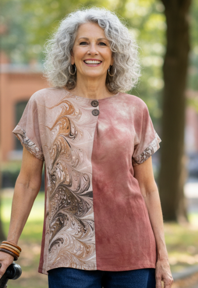 Woman standing on a park bench wearing a marbled silk top and blue jeans, with trees and buildings in the background.