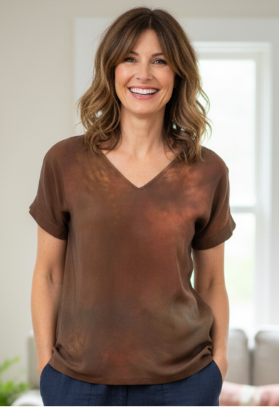 Woman wearing a hand dyed brown shirt and blue pants standing in a living room.