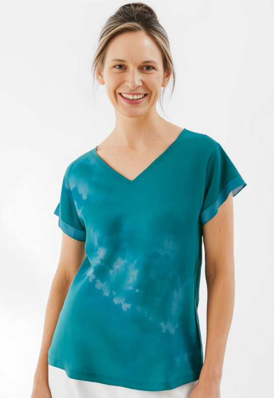 Woman wearing a teal tie-dye shirt and white pants on a white background