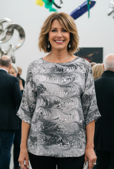 Woman wearing a black and white marbled silk top standing in an art gallery with colorful sculptures in the background