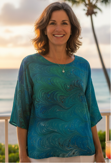 Woman in an emeralds marbled silk top standing by a beach with palm trees and sunset.