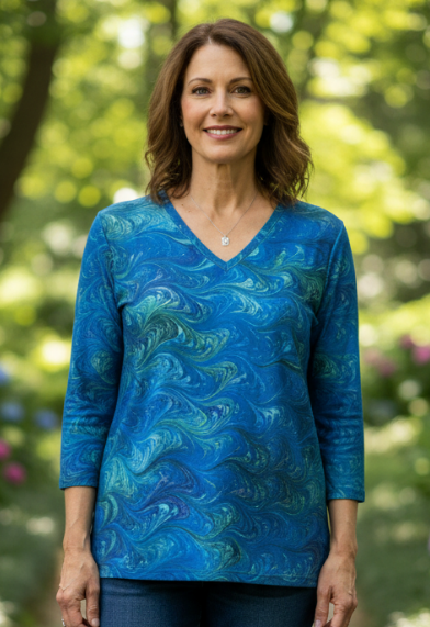 Woman wearing a blue cotton marbled top and jeans standing on a stone path with greenery and flowers in the background