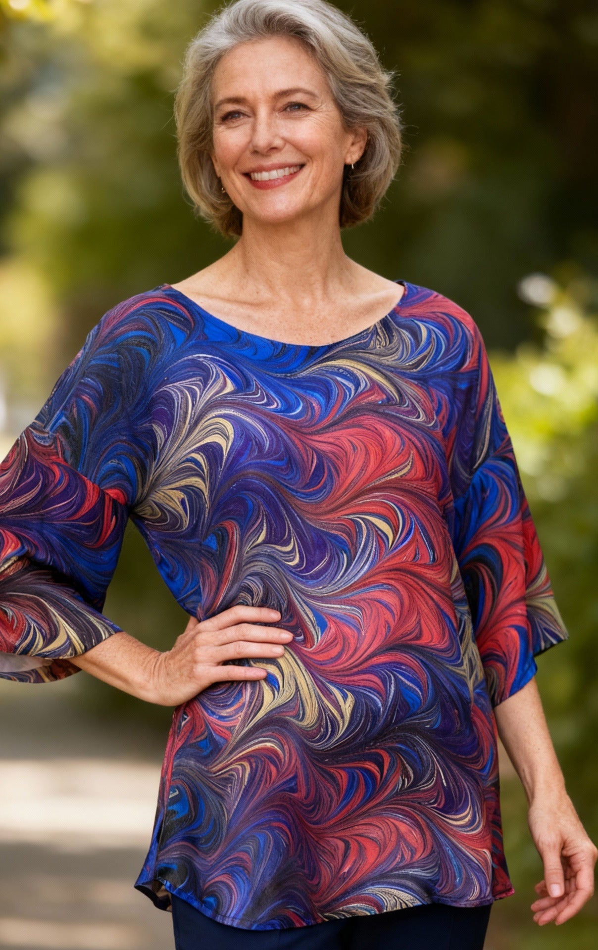 Woman wearing a colorful marbled silk top outdoors with greenery in the background