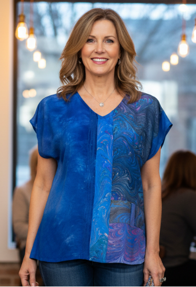 Woman wearing a blue one of a kind silk top and jeans in an indoor setting with brick walls and hanging lights.