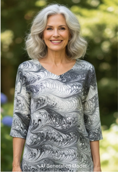 Woman wearing a black and white half sleeve v neck silk top standing on a garden path surrounded by flowers