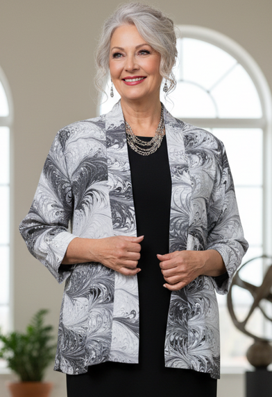 woman wearing a marbled silk black and white swing jacket over a black dress standing in a bright room