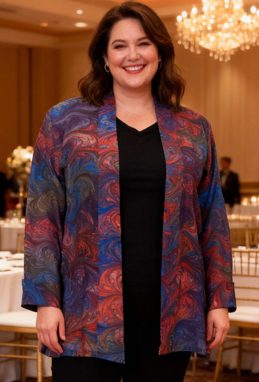 Woman in a colorful hand marbled silk swing jacket standing in a banquet hall with tables and chandeliers.