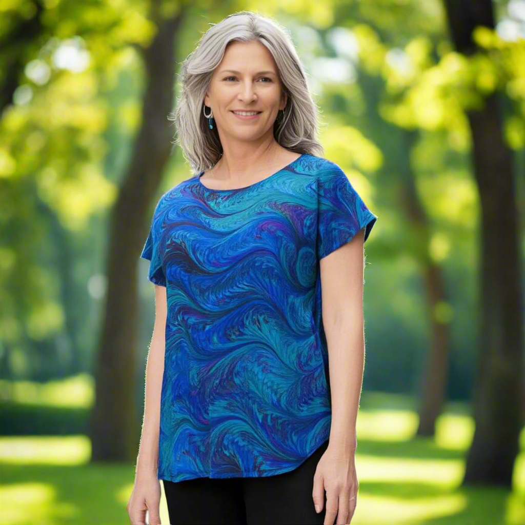 Woman wearing a short sleeve, marbled, blue and aqua silk Blouse against a background of a park