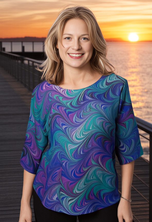 Woman wearing a marbled silk shirt standing on a dock at sunset.