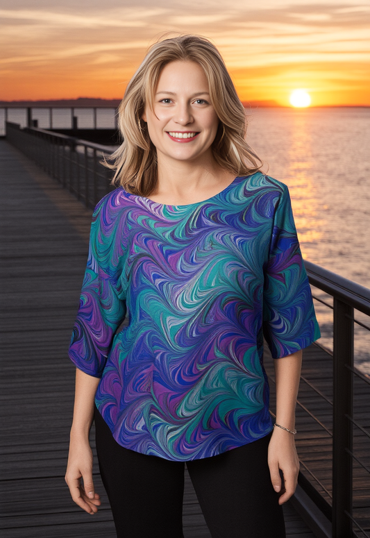 Woman wearing a marbled silk shirt standing on a dock at sunset.