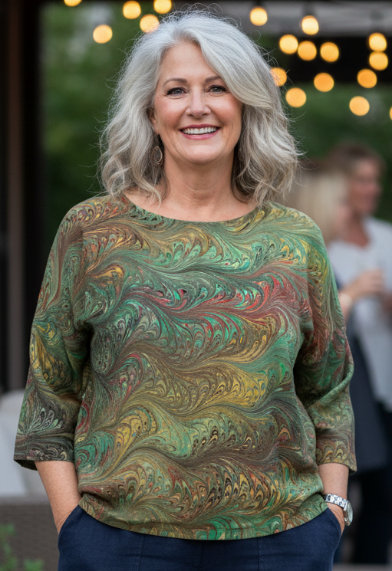 Woman wearing a marbled silk  top in warm green and golden tones standing outdoors 