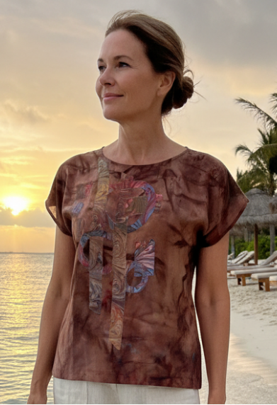 Woman wearing a hand dyed brown shirt with sewn applique graphic standing on a beach at sunset 