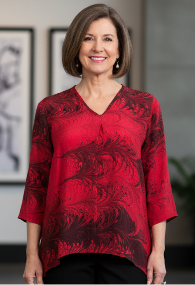 Woman wearing a red marbled silk blouse and black pants in an indoor setting.