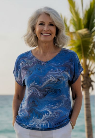 Woman wearing a blue and purple marbled silk shirt by the ocean with palm trees in the background