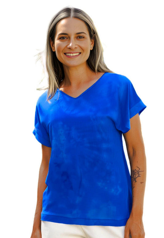 Woman wearing a blue hand dyed silk shirt and white pants on a white background