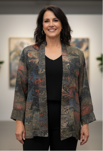 Woman wearing a marbled silk swing jacket over a black top and pants in an indoor setting with plants and artwork.