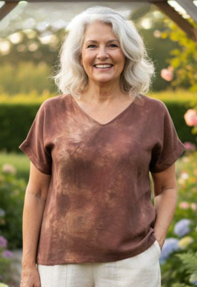Woman wearing a hand dyed brown shirt standing outdoors with greenery in the background