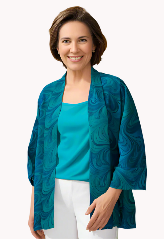 Woman wearing a blue marble sheer  jacket over a turquoise top and white pants with ocean view in background