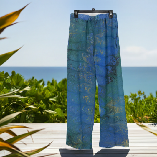 Light blue and green marbled silk pants against the backdrop of an ocean scene with tropical plants