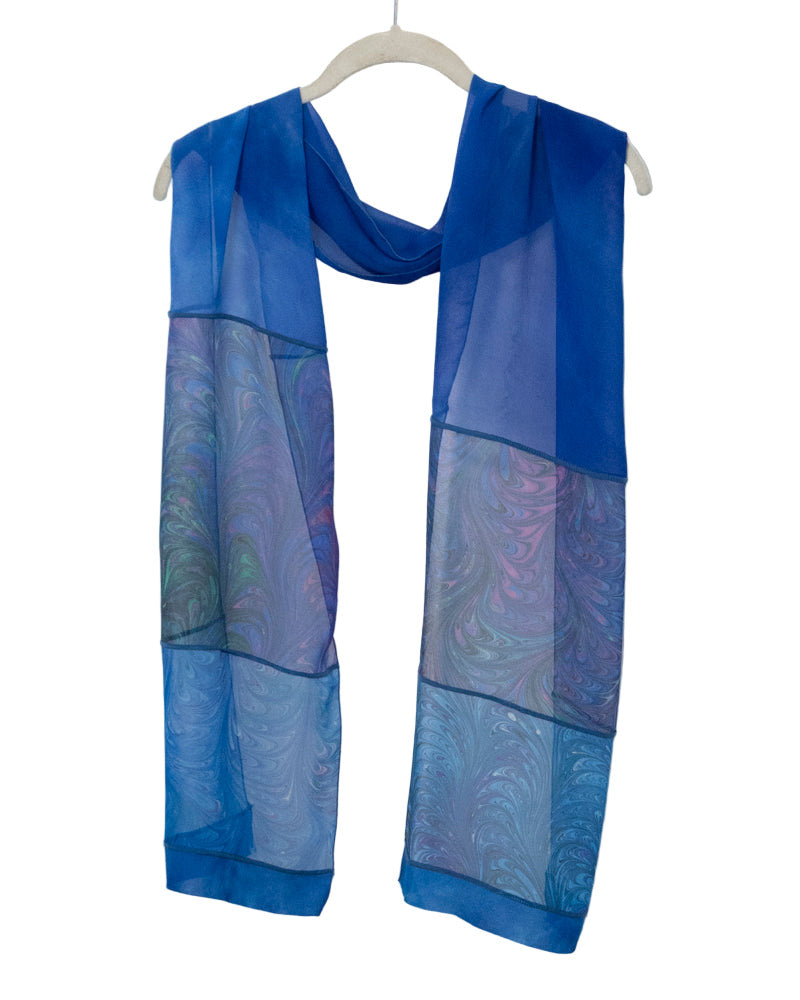 Blue marbled silk scarf draped over a hanger on a white background
