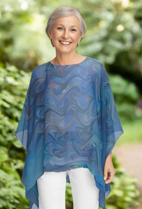 Woman wearing sheer blue poncho with white pants with trees in background
