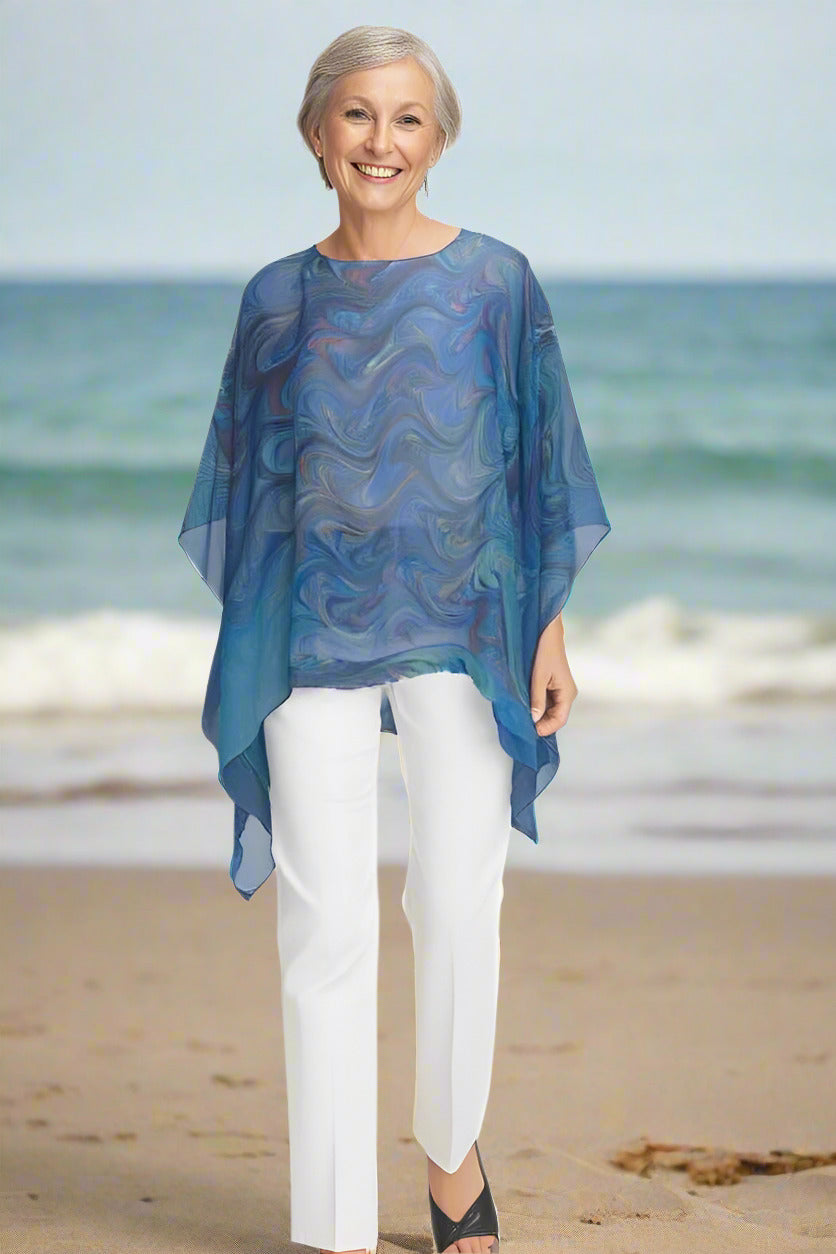 Woman wearing sheer blue poncho with white pants walking on the beach